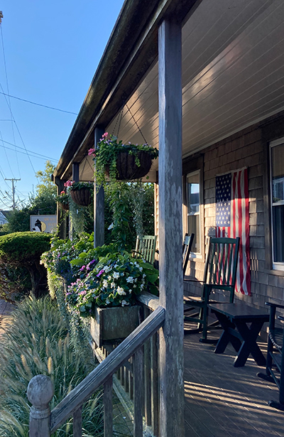 Nantucket coastal porch with cedar shingles, rocking chairs, hanging flower baskets, and American flag